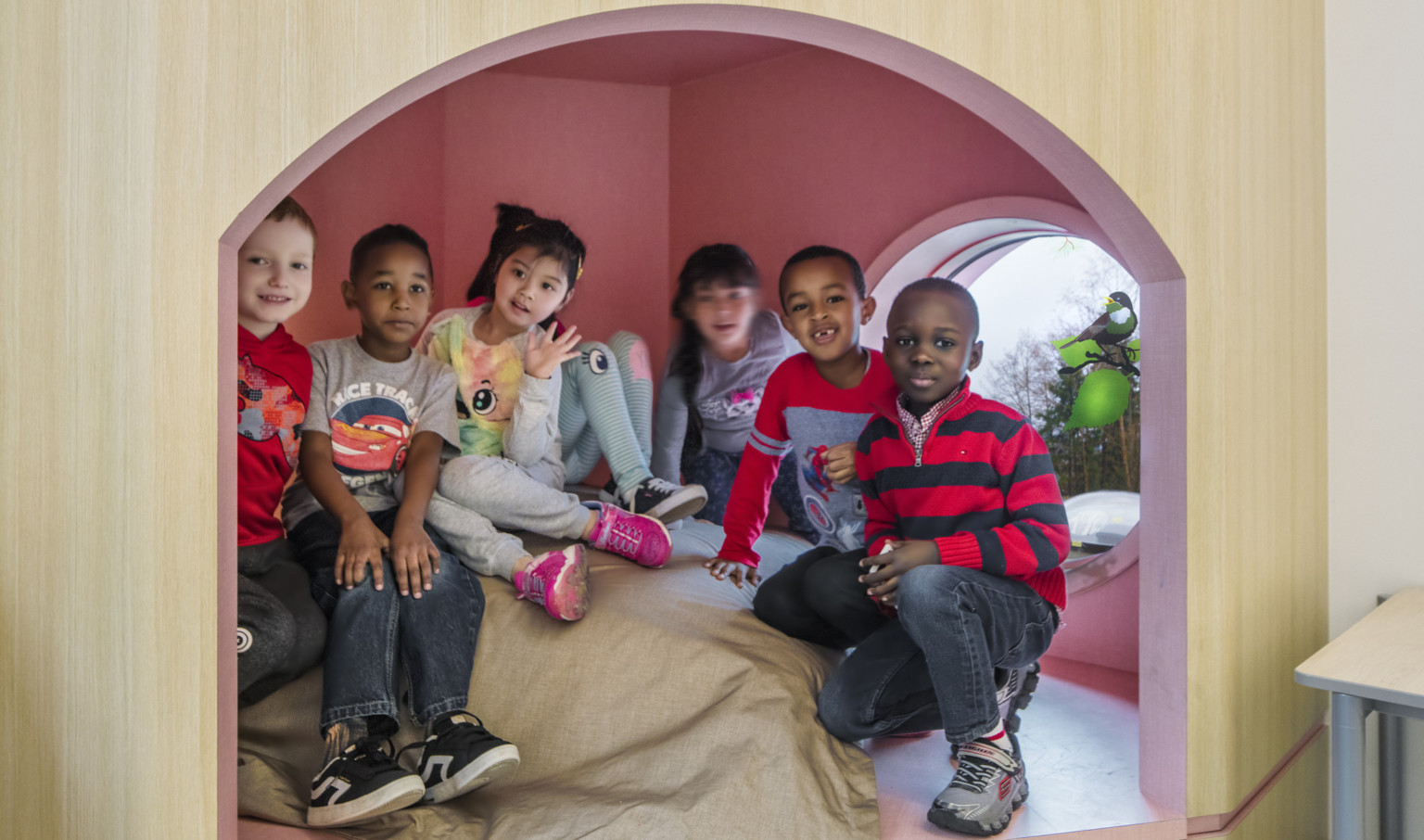 Students gathered in enclosed padded play area with arched small wood doorway