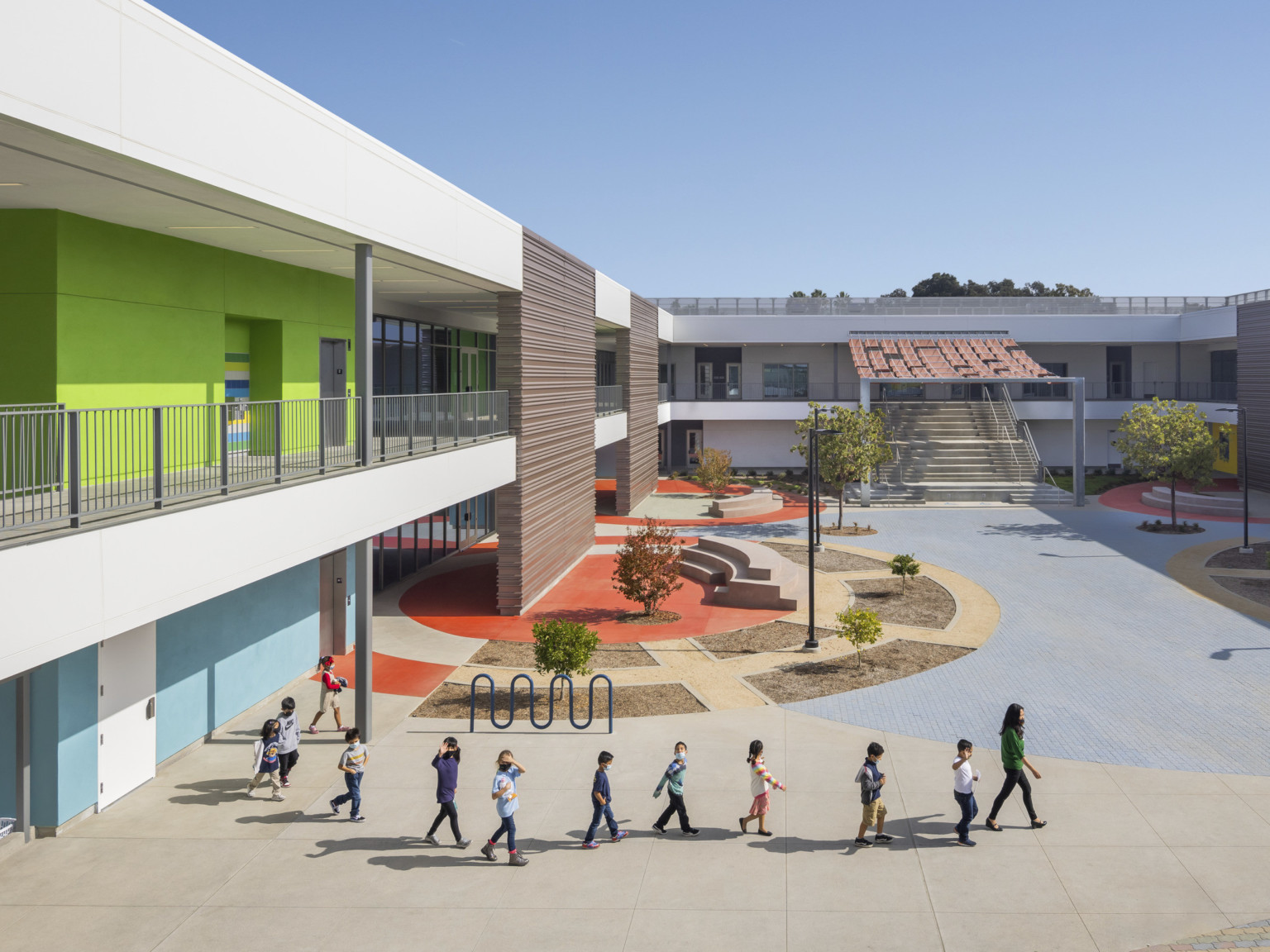 Exterior courtyard, blue and green walls to left with white walkway and canopy. Round orange accent on ground