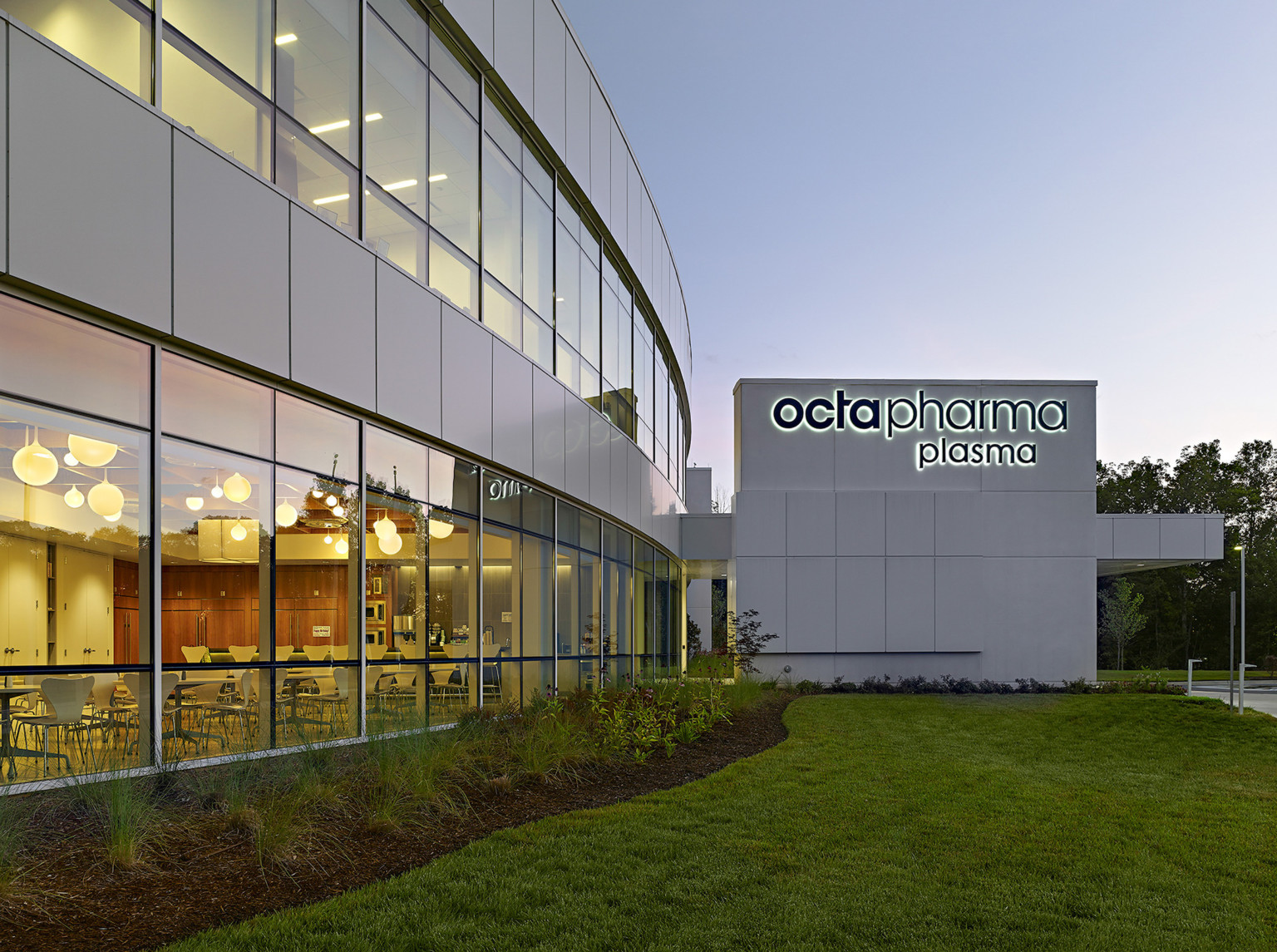 evening view of a double height glass facade with Octapharma logo on the far building wall