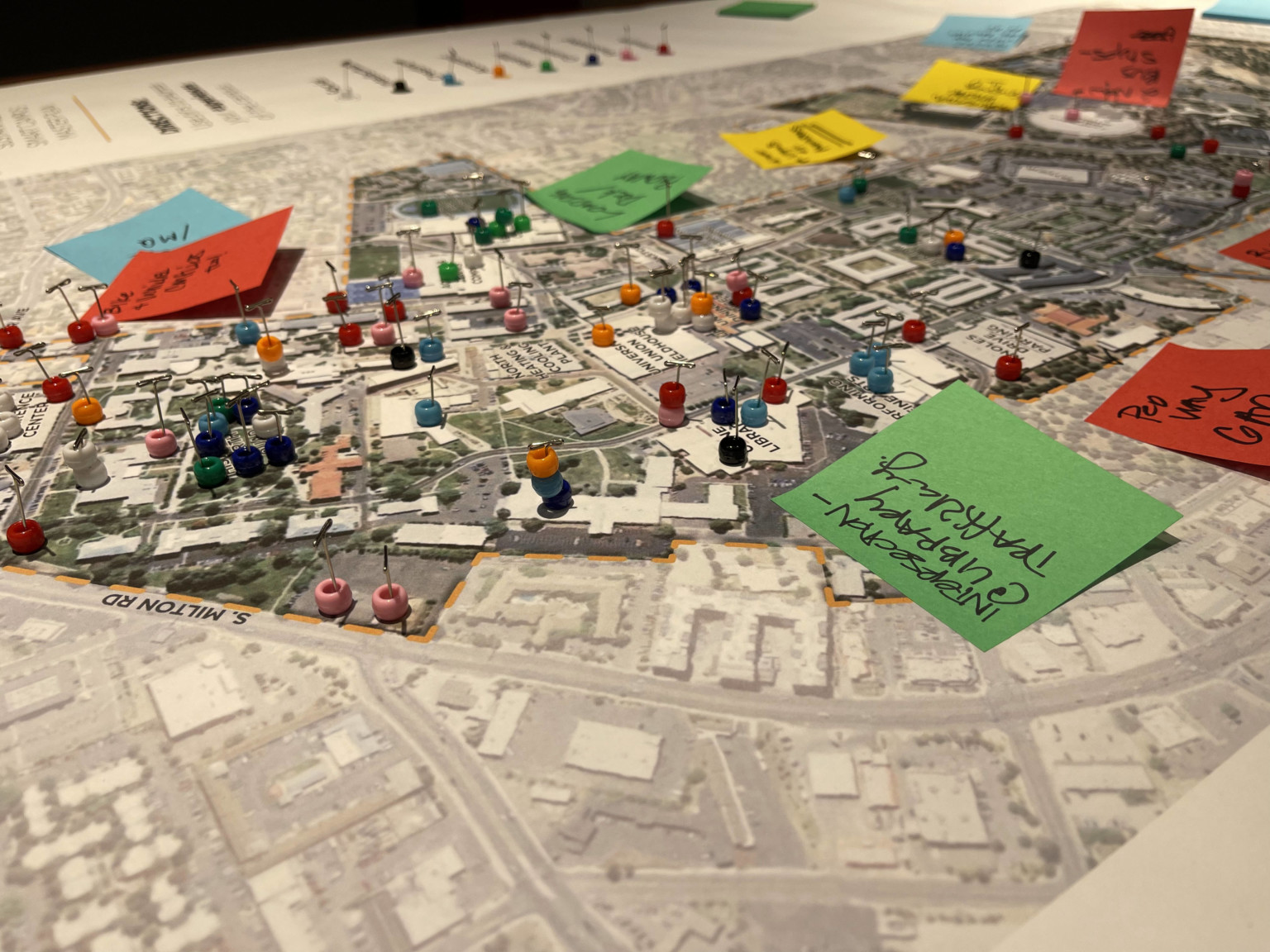 master plan poster with buildings, trees, and streets shown in color. colorful post-its and beads pinned across mark up