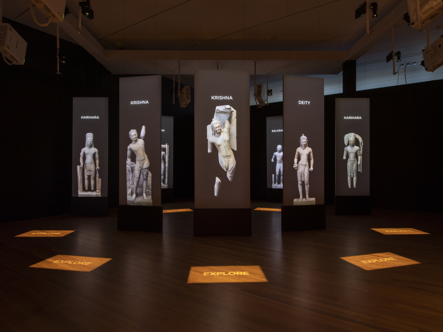 a darkened room with screens and stone statue images suspended in a circle pattern with illuminated signage on the wood floor