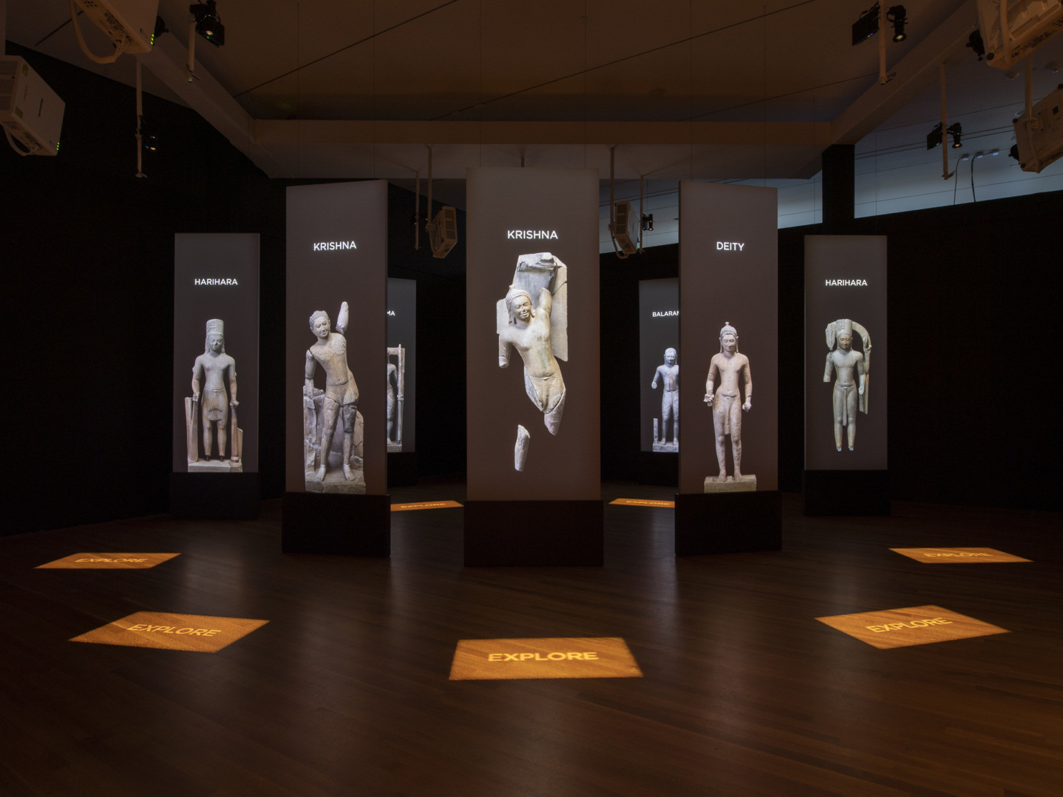 a darkened room with screens and stone statue images suspended in a circle pattern with illuminated signage on the wood floor a darkened room with screens and stone statue images suspended in a circle pattern with illuminated signage on the wood floor