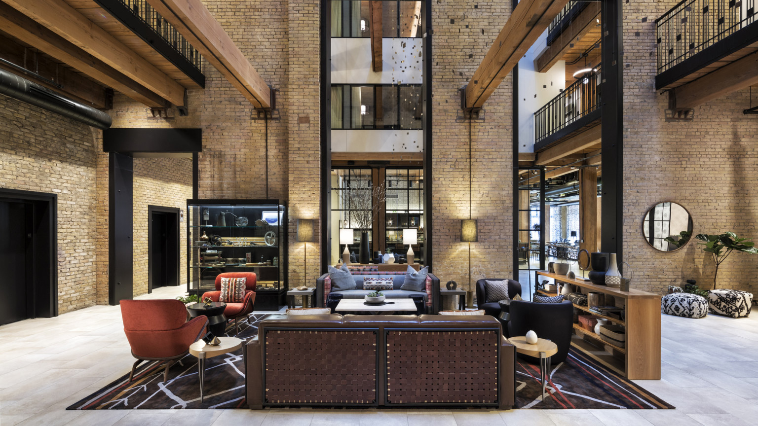Interior atrium with exposed brick. Seating area at center and wood beams overhead. 2 walkways on sides above with metal rail Interior atrium with exposed brick. Seating area at center and wood beams overhead. 2 walkways on sides above with metal rail