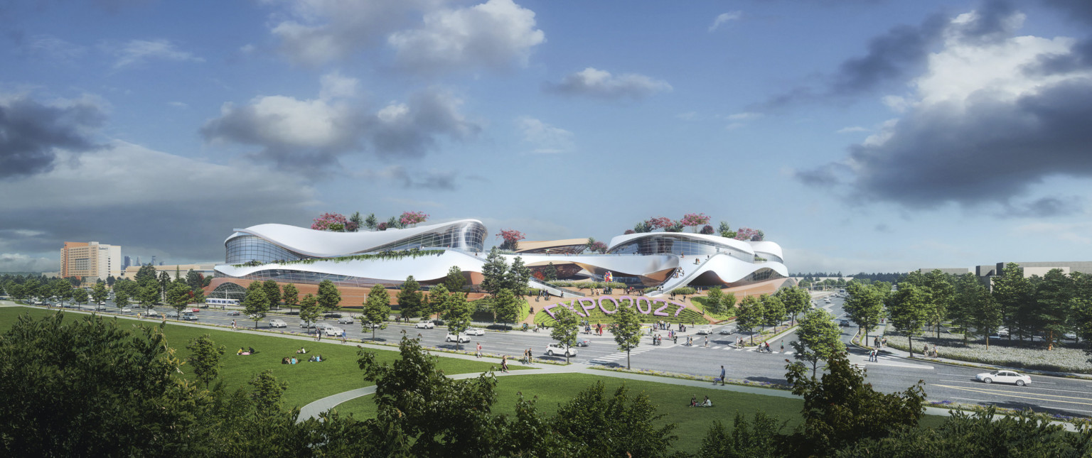 White building with rounded flowing walls and multiple stories in green space with lots of trees and Expo 2027 sign