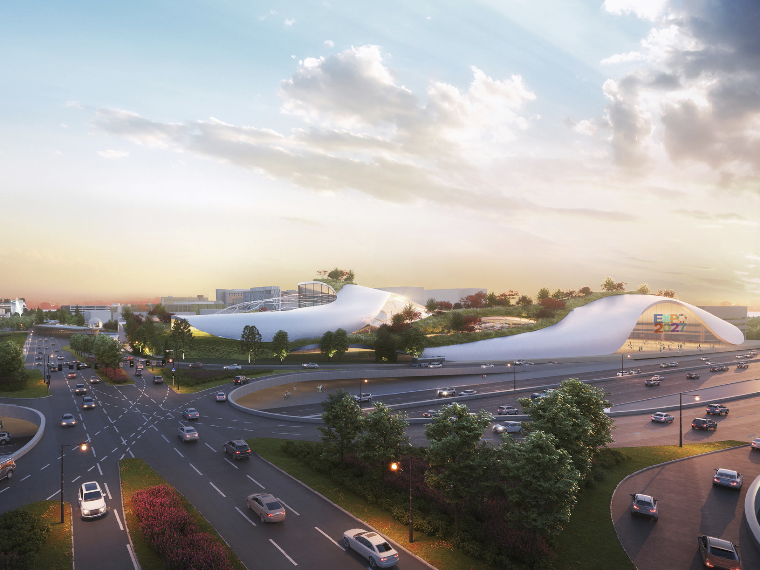 White building with rounded flowing walls and multiple stories in green space with lots of trees at intersection of roads
