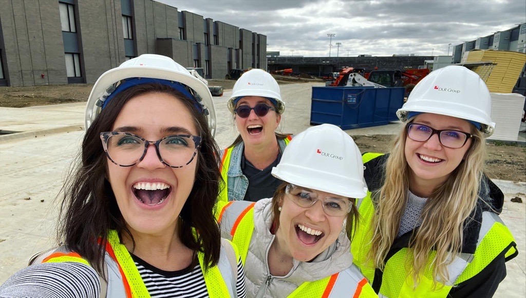 four women in hard hats and reflective vests on a construction site taking a selfie