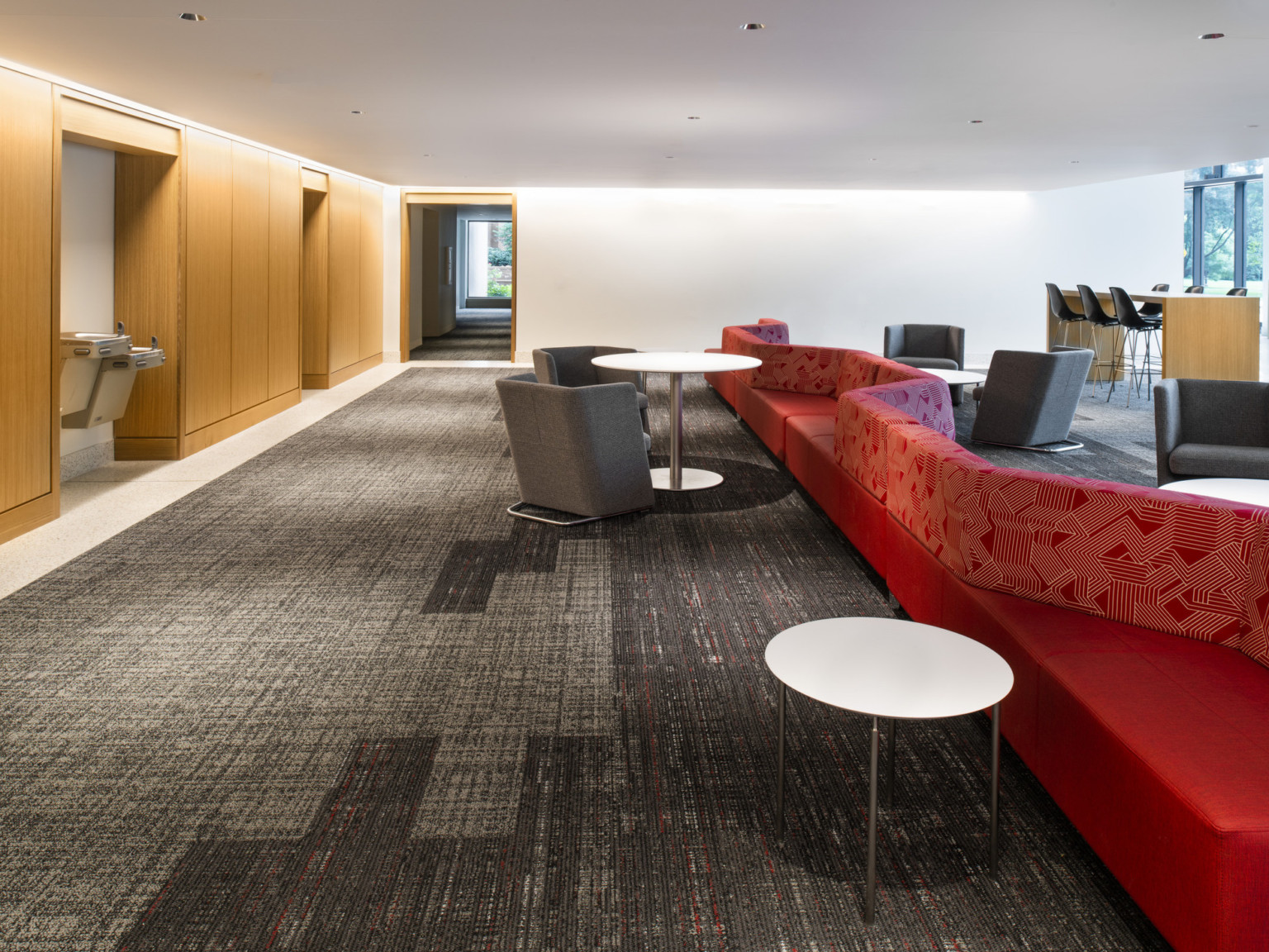 Mixed seating in common space lobby with counters, red geometric double-sided sofa, armchairs. Wood hidden cabinets, left