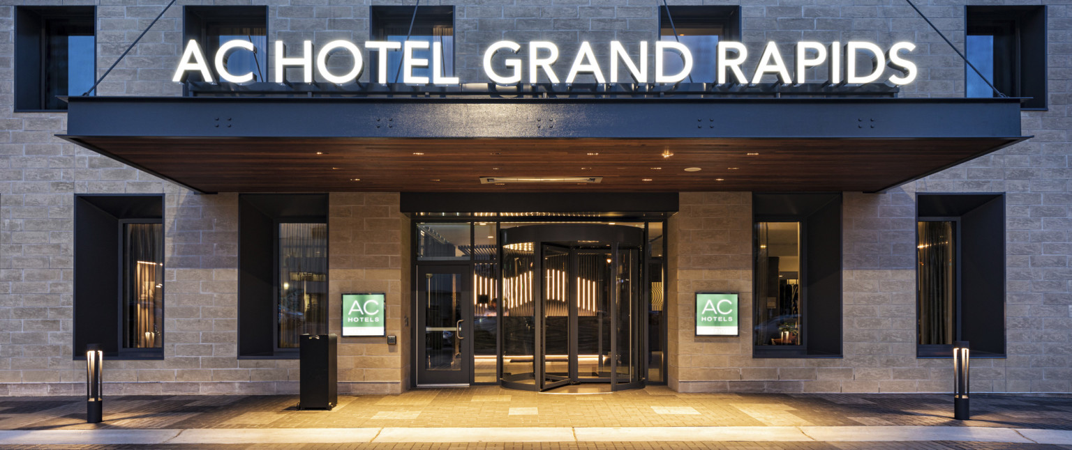 Close up of hotel entry with name illuminated above and signage on stone walls on either side of revolving door