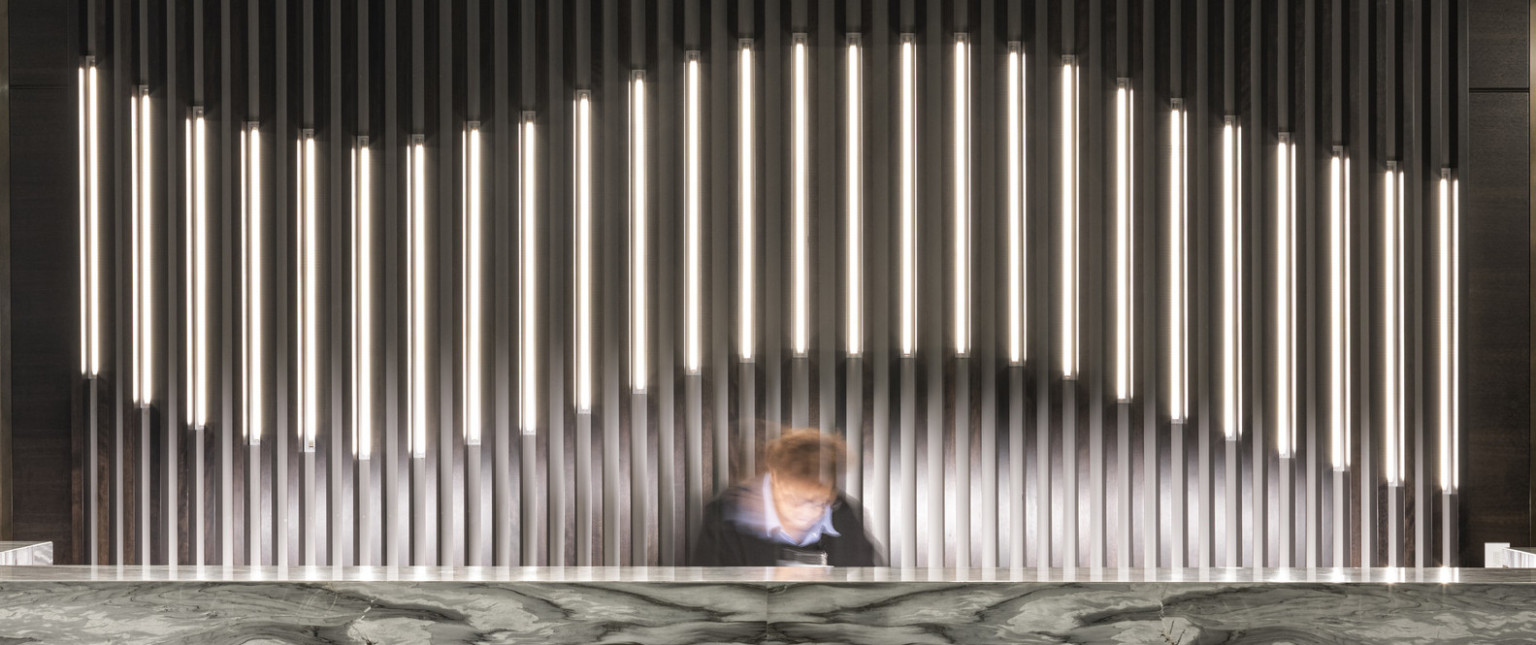 Dark marbled reception desk in lobby with thin pillared wall details, partially illuminated curve along center
