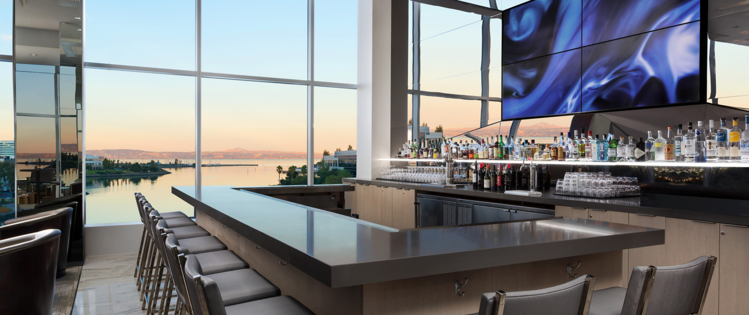 Wood bar with grey counter in room with floor to ceiling windows in front of mirror with central abstract swirling panels