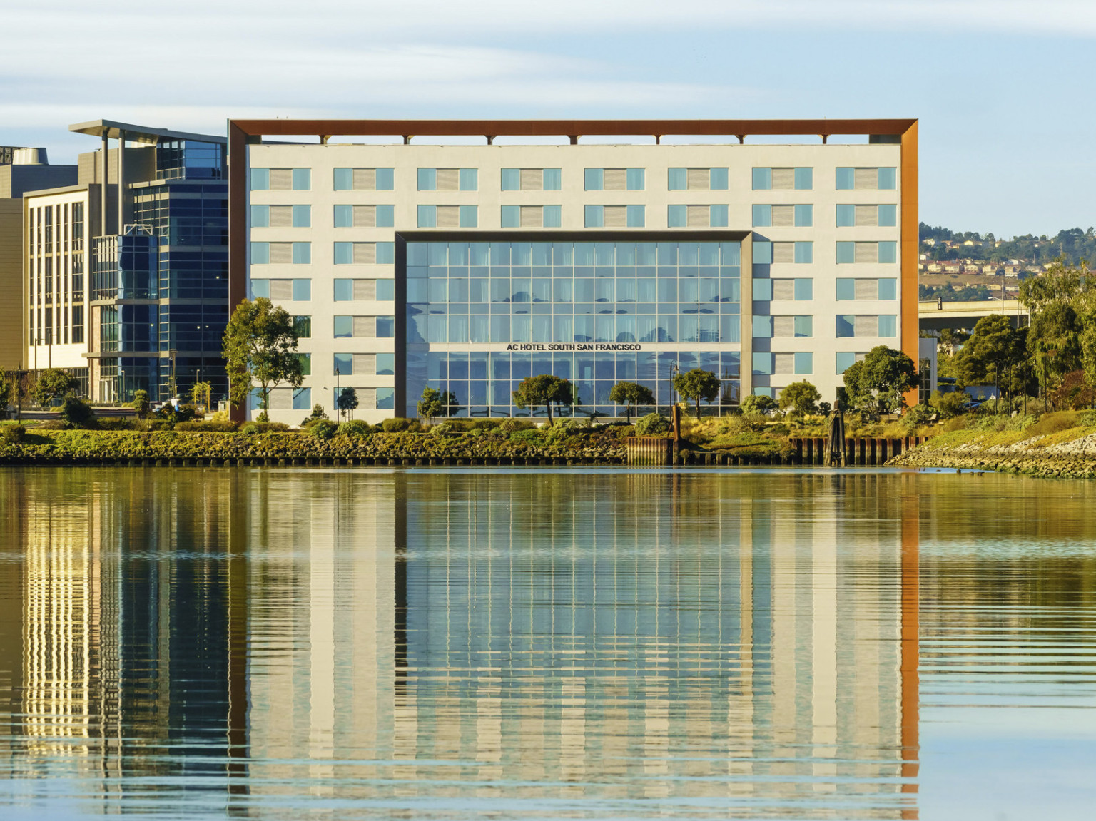 View of hotel entry across the water. The 7 story building has recessed section of floor to ceiling windows at center