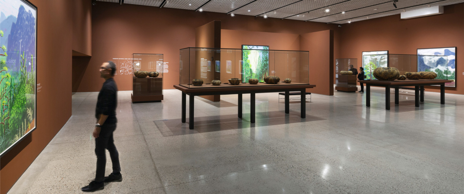Orange brown gallery walls with vibrant green visual displays hanging on them. Native American pottery on display at center