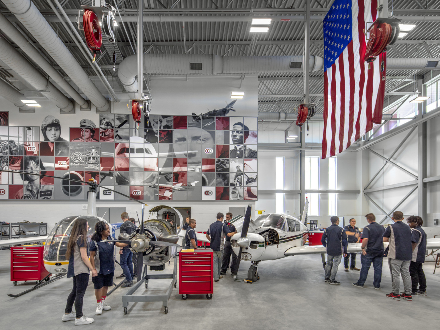 Aviation lab with helicopter, small plane, and displayed engine. Mural at back with planes and pilots. American flag, right