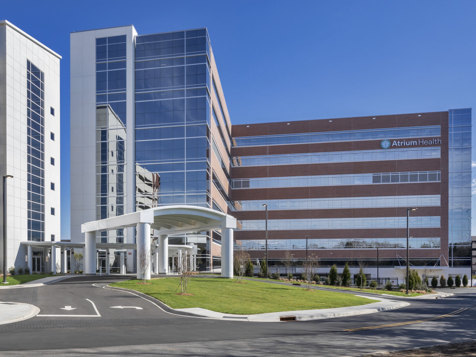 Atrium Health Pineville Bedtower Expansion. A multistory tower with white arching carport over drive. Garage to left Atrium Health Pineville Bedtower Expansion. A multistory tower with white arching carport over drive. Garage to left