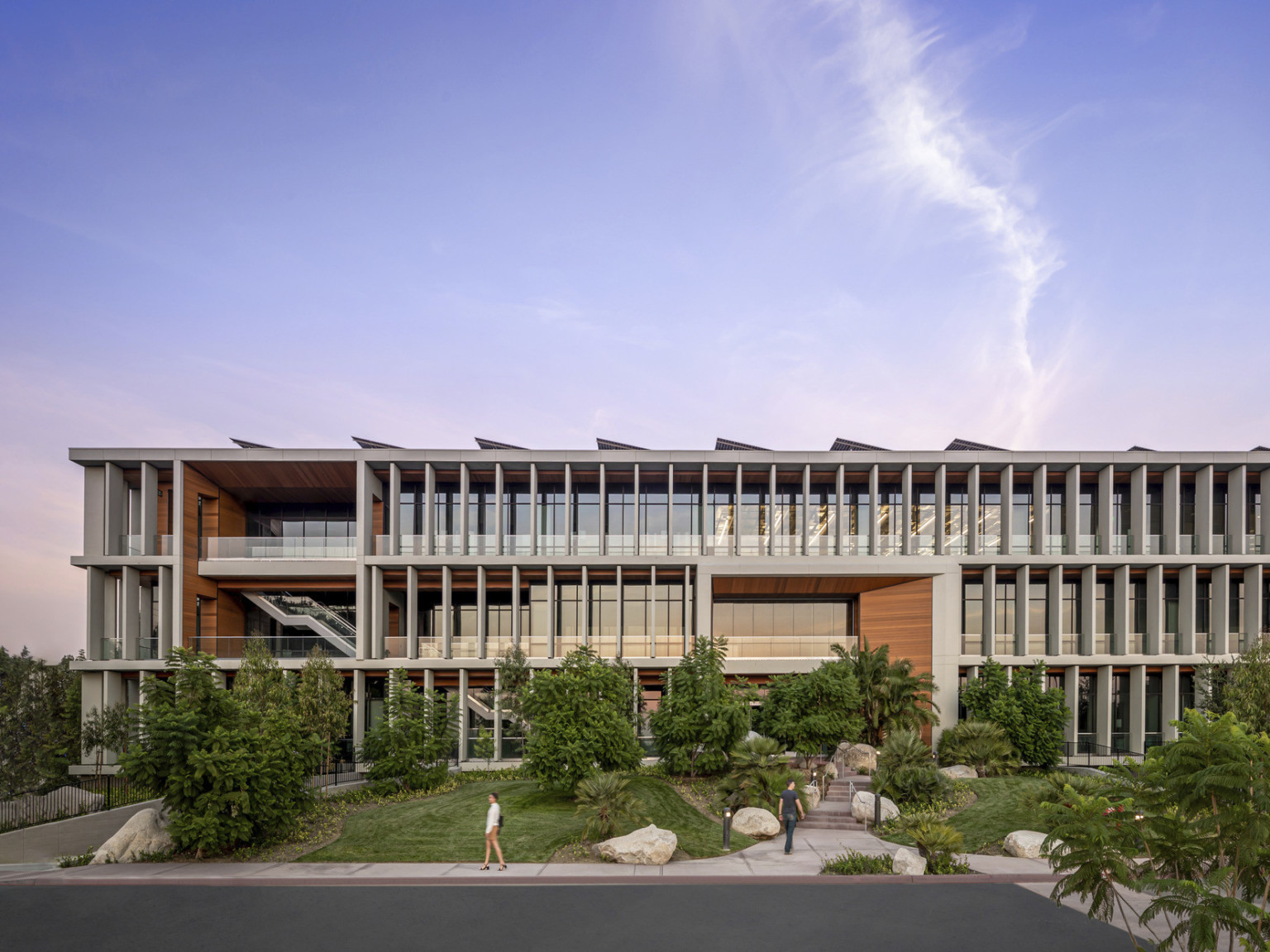 White wrapped slat facade with wood accents over above grade glass building. Lawn with large plants slopes up to building