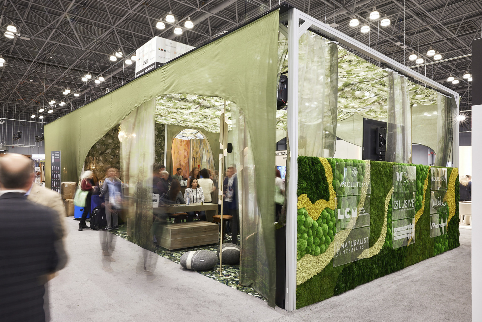 Exterior corner view of DLR Group's BDNY 2022 convention booth with textural living wall and green drapes around seating area