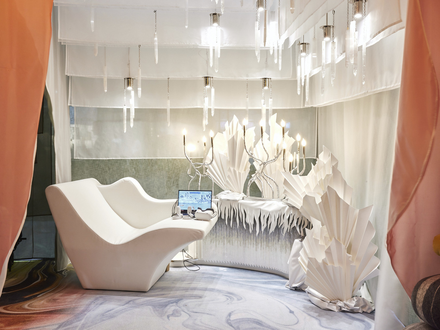 All white wintery room with ice shard style sculptures and organically curving candelabra lights framed by peach toned curtains