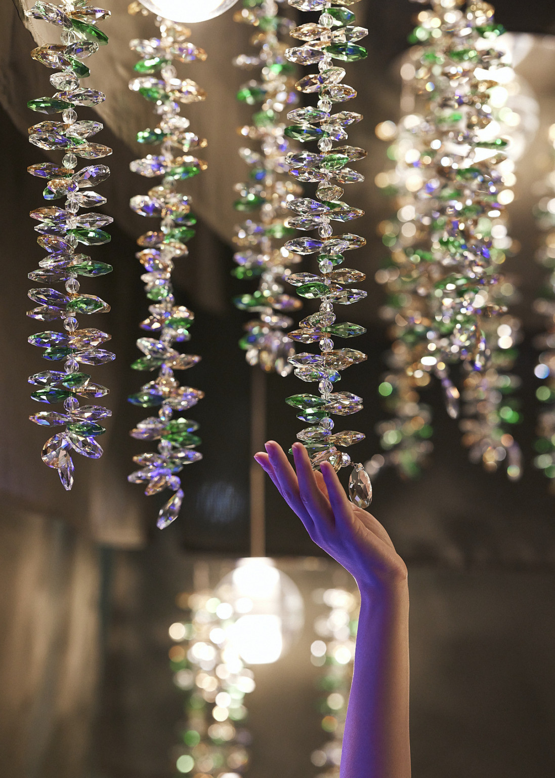 Hand reaches up to touch purple, green, and yellow tinted glass bead strands hanging from pendant lights