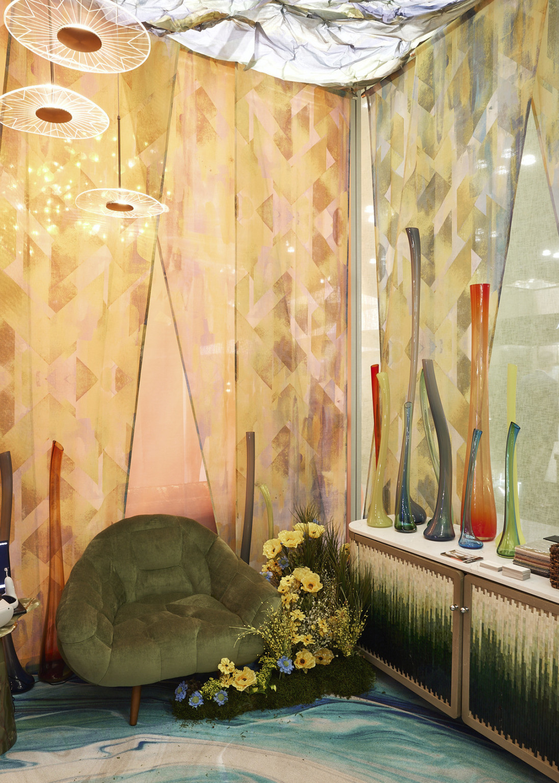 Corner with geometric patterned curtains on each wall. Warm tones left, cool right. Tall curved vases, green chair and flowers