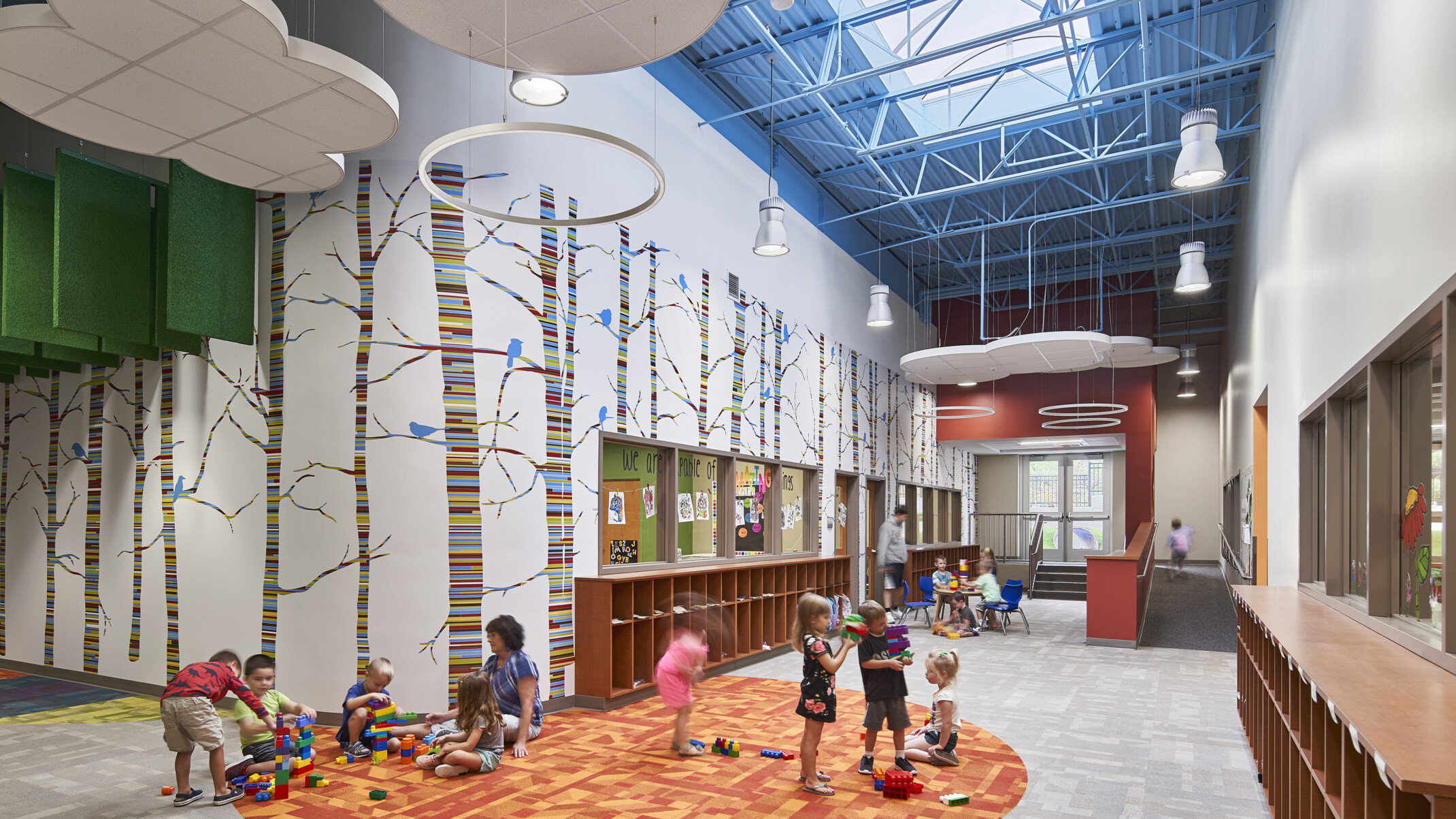 Kearney Early Childhood Education Center learning hallway with striped tree mural and hanging cloud accents under skylight