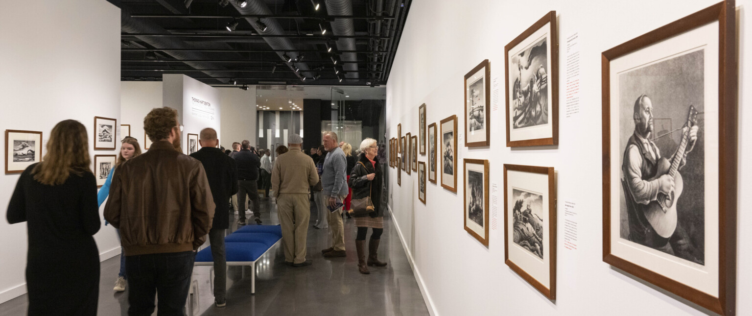 People observing art in an art gallery with white walls and black ceiling, walls are filled with photographs