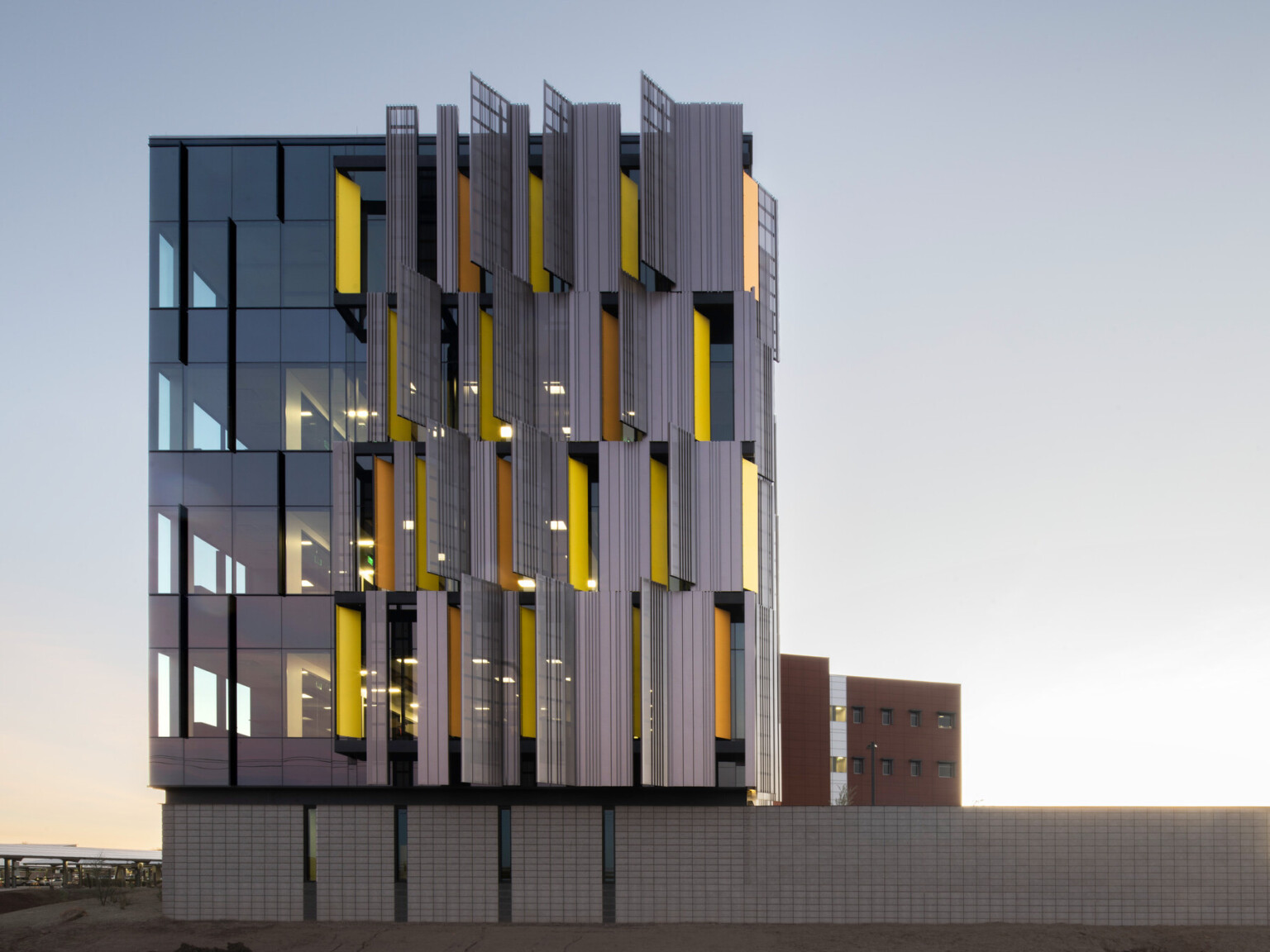 side view of courthouse with serrated sunscreen facade, a pattern of yellow panels peaking between. Floor to ceiling windows
