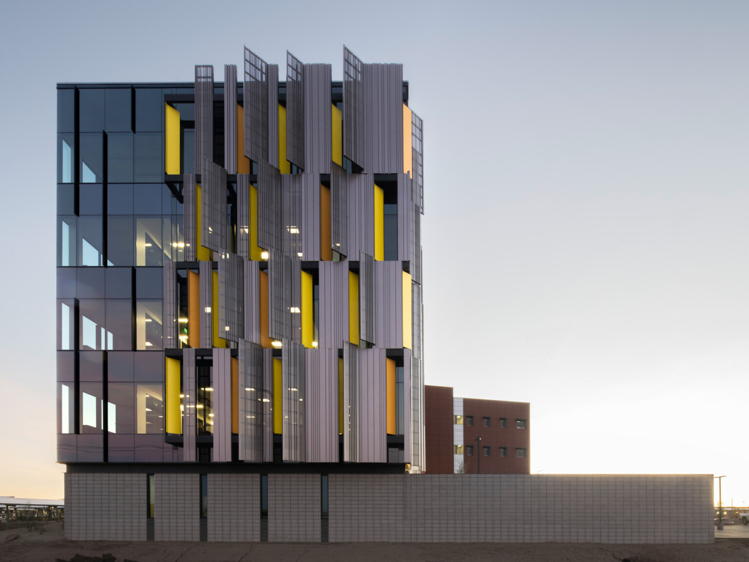 side view of Pinal County Attorney's Office with serrated sunscreen facade, a pattern of yellow panels peaking between. Floor to ceiling windows