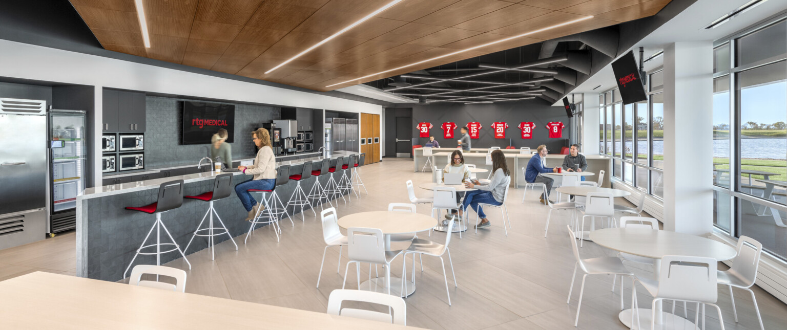 Gray and red finishes, stone flooring, and a wood ceiling bring to life the large cafe with multiple seating options with views to the exterior and lake.