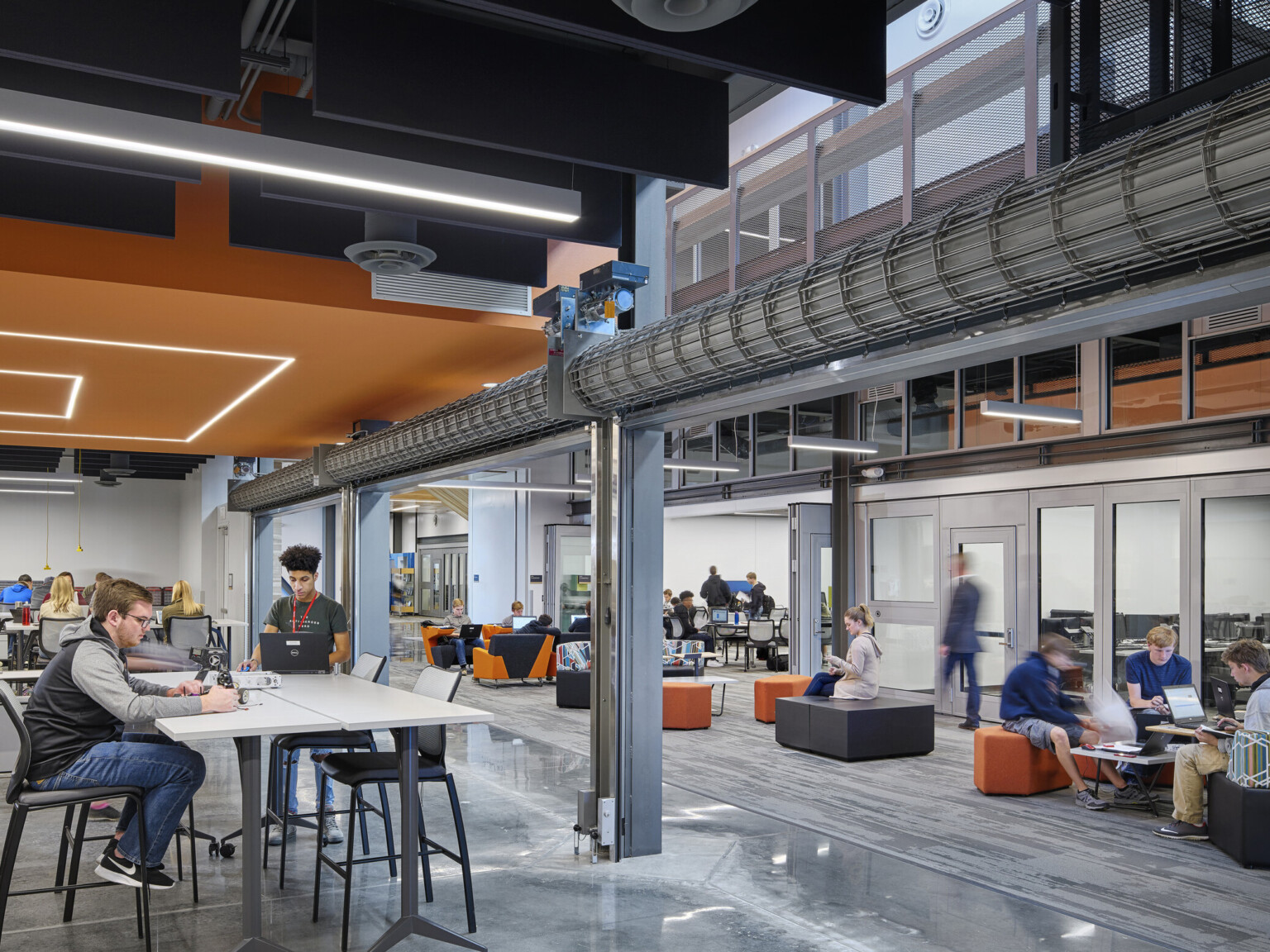 Large commons space with seating under a black ceiling and a geometric orange drop ceiling detail with recessed lights