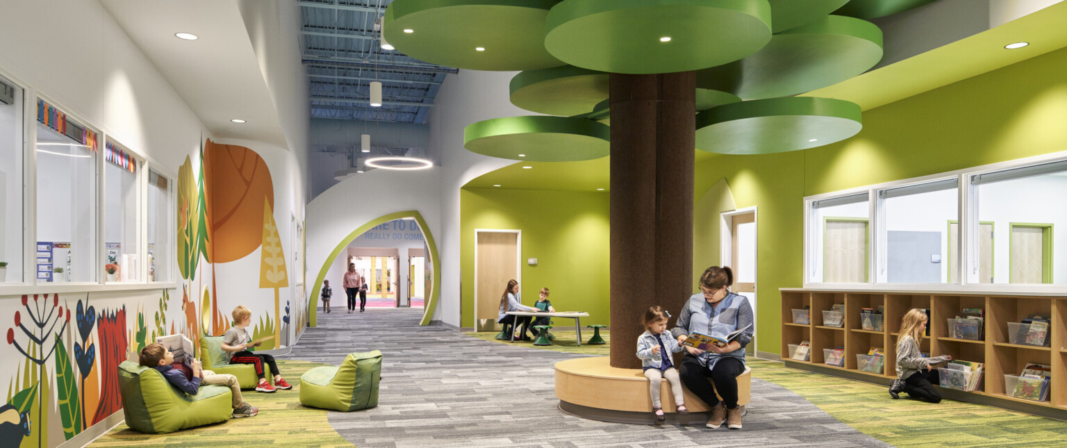 people reading on a brown circular bench with a brown column and green ceiling fixtures in hallway lined with forest graphics