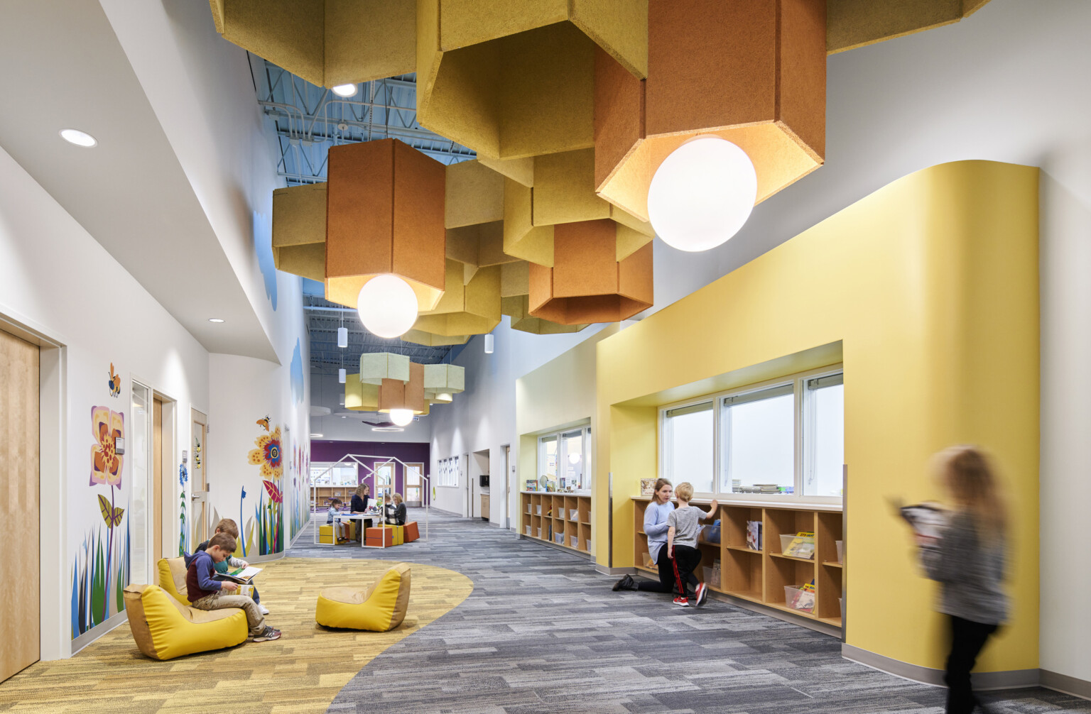 Hallway with comfortable soft seating, yellow wall and carpet accents. Yellow pentagonal baffles and globe pendant lights