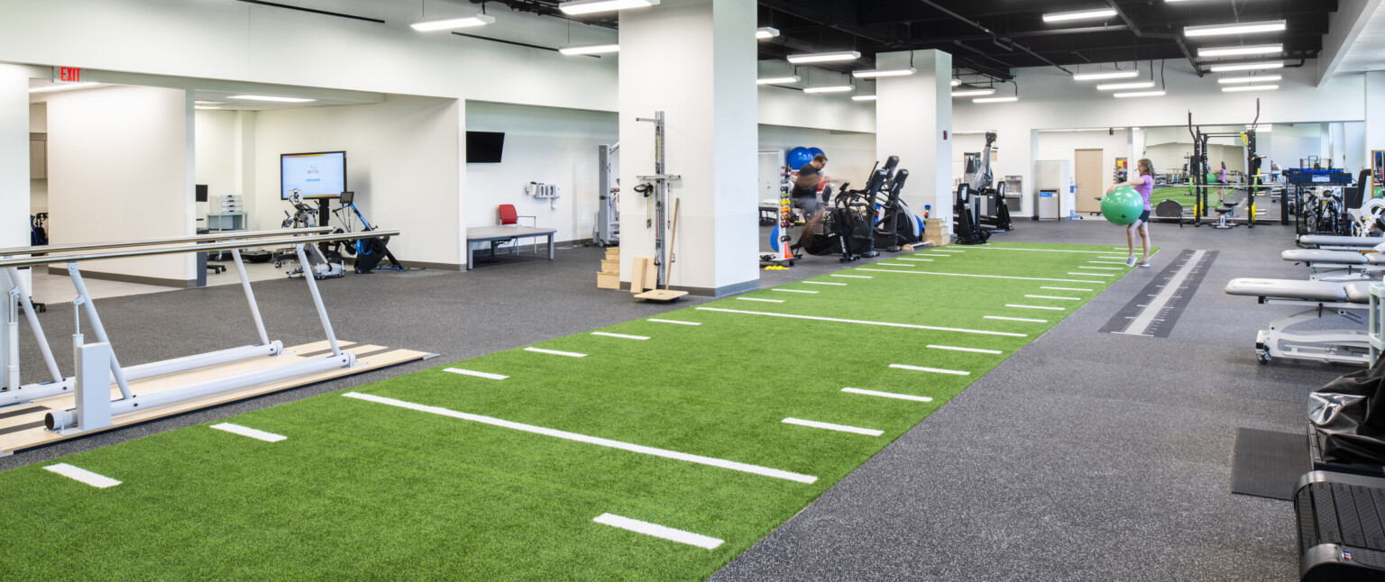 Exercise room with mixed equipment, green faux football field strip with yards marked runs down center of room