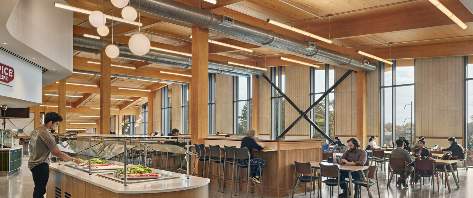 Dining area with flexible seating below wood ceiling with beam details, hanging rod lights, fireplace with white chimney back