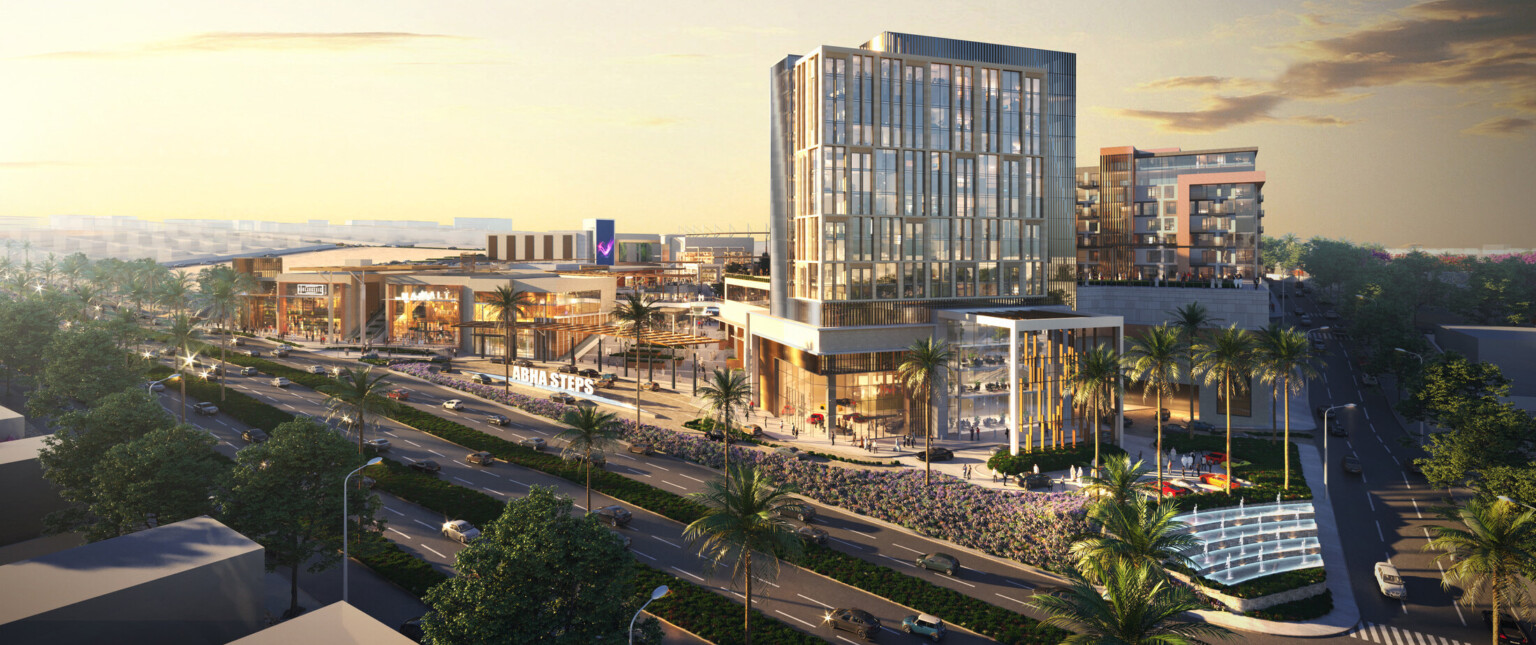 View of shopping center from across the street, midrise building to right towering over stores and courtyard