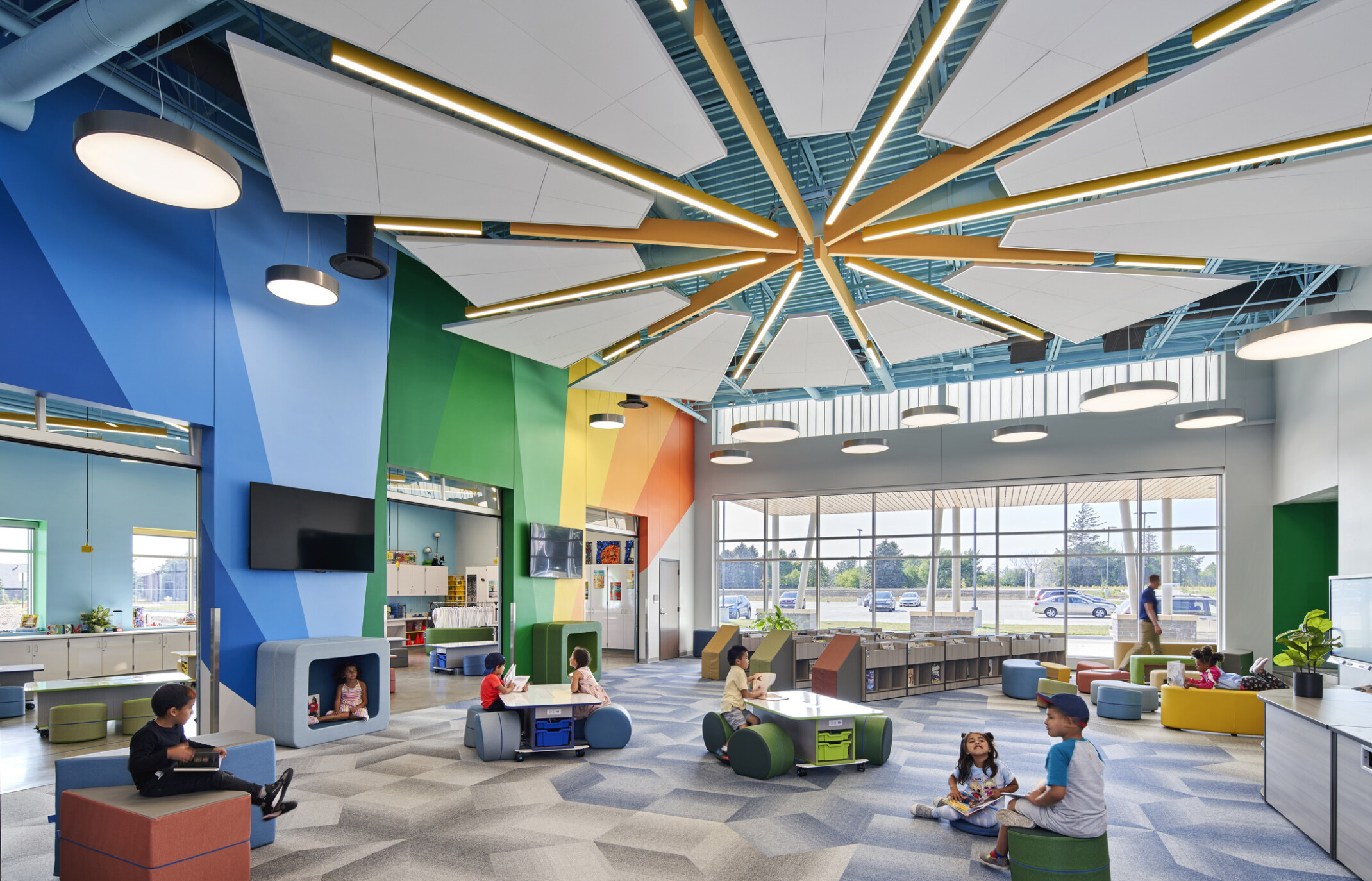 Classroom interior mixed-purpose room with vaulted ceilings, colorful beams, brightly colored walls, natural daylight, children seated in modern ergonomic chairs