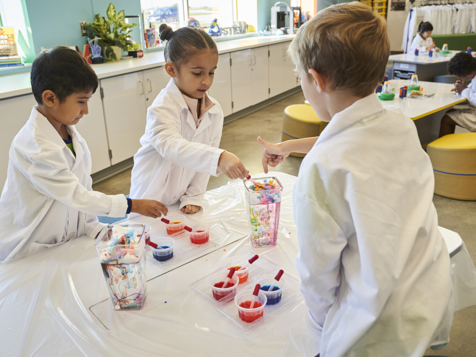 Children in white lab coats collaborating on art project