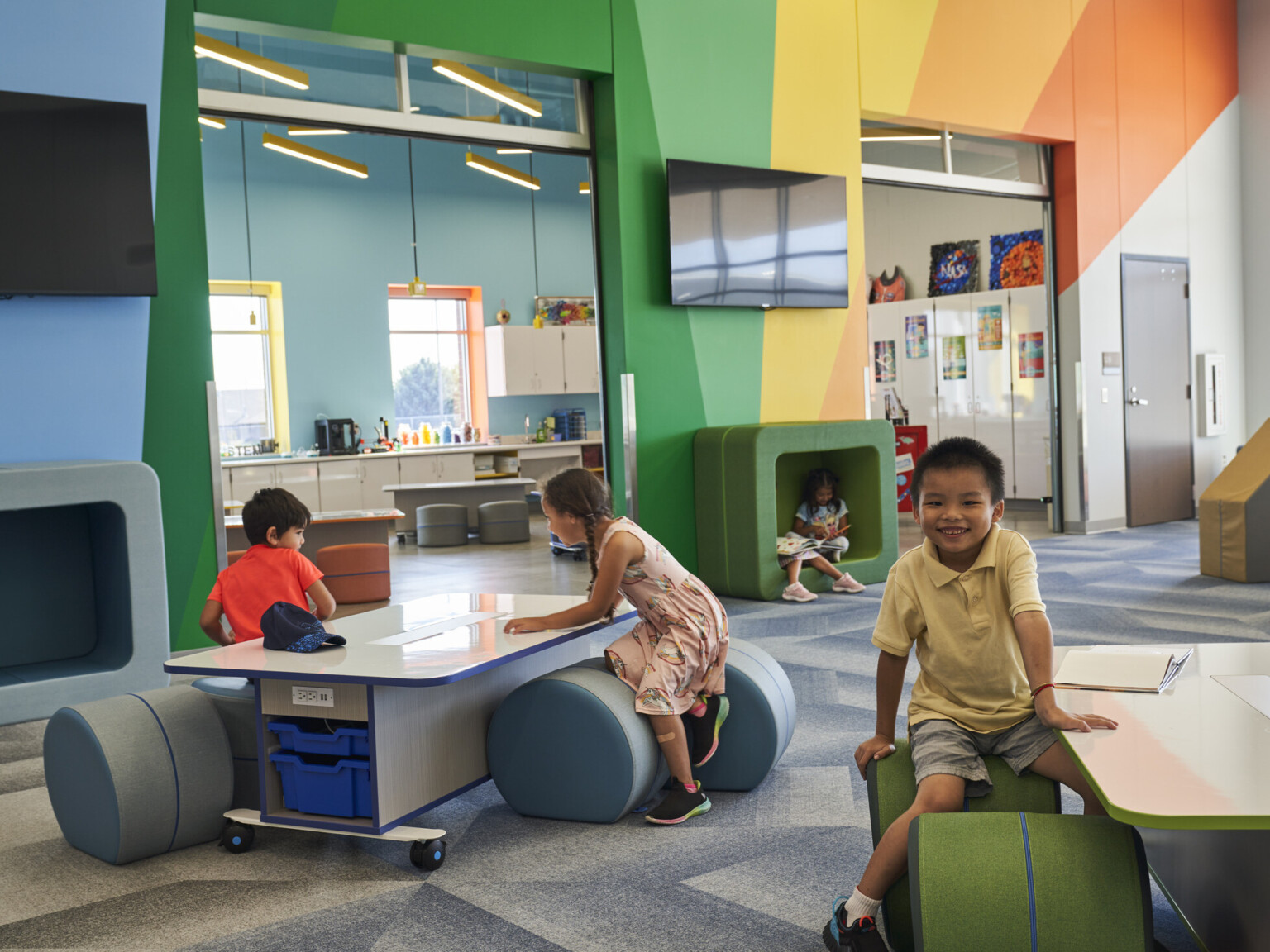 Children in classroom with brightly painted walls, modern aesthetic, vaulted ceilings and colorful ergonomic seating arrangement
