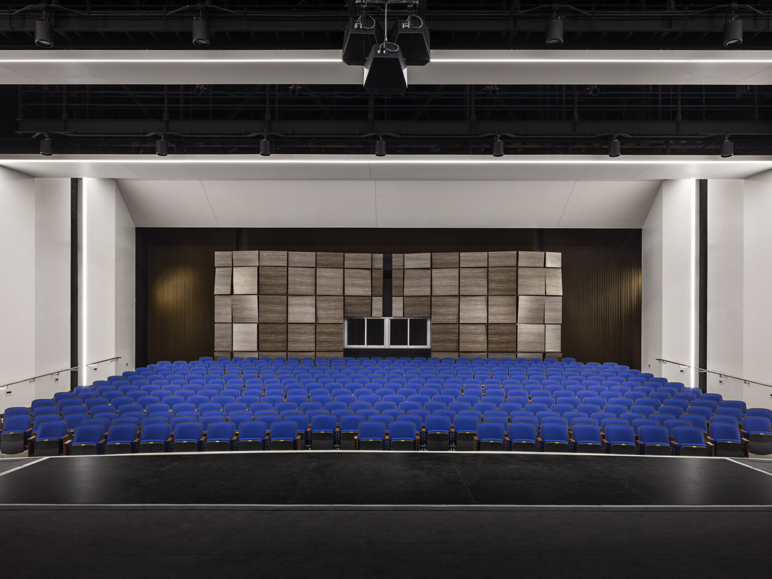 View from stage looking towards audience chamber with blue eats and white walls, textured acoustical panels on back wall