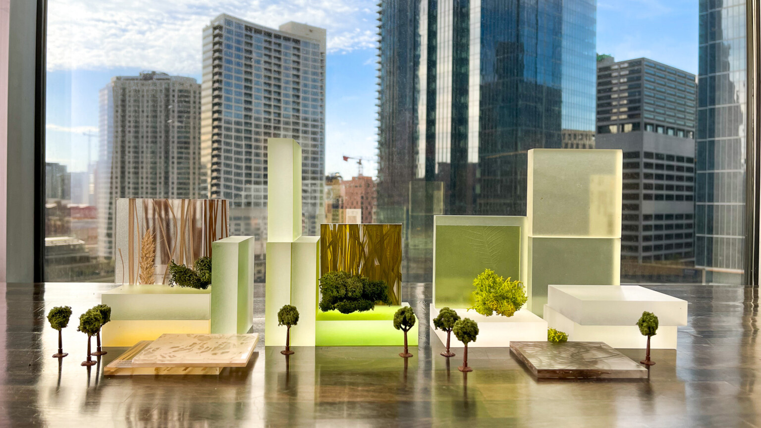 green toned abstract clear models of building with scale trees in front of window, view of high rises